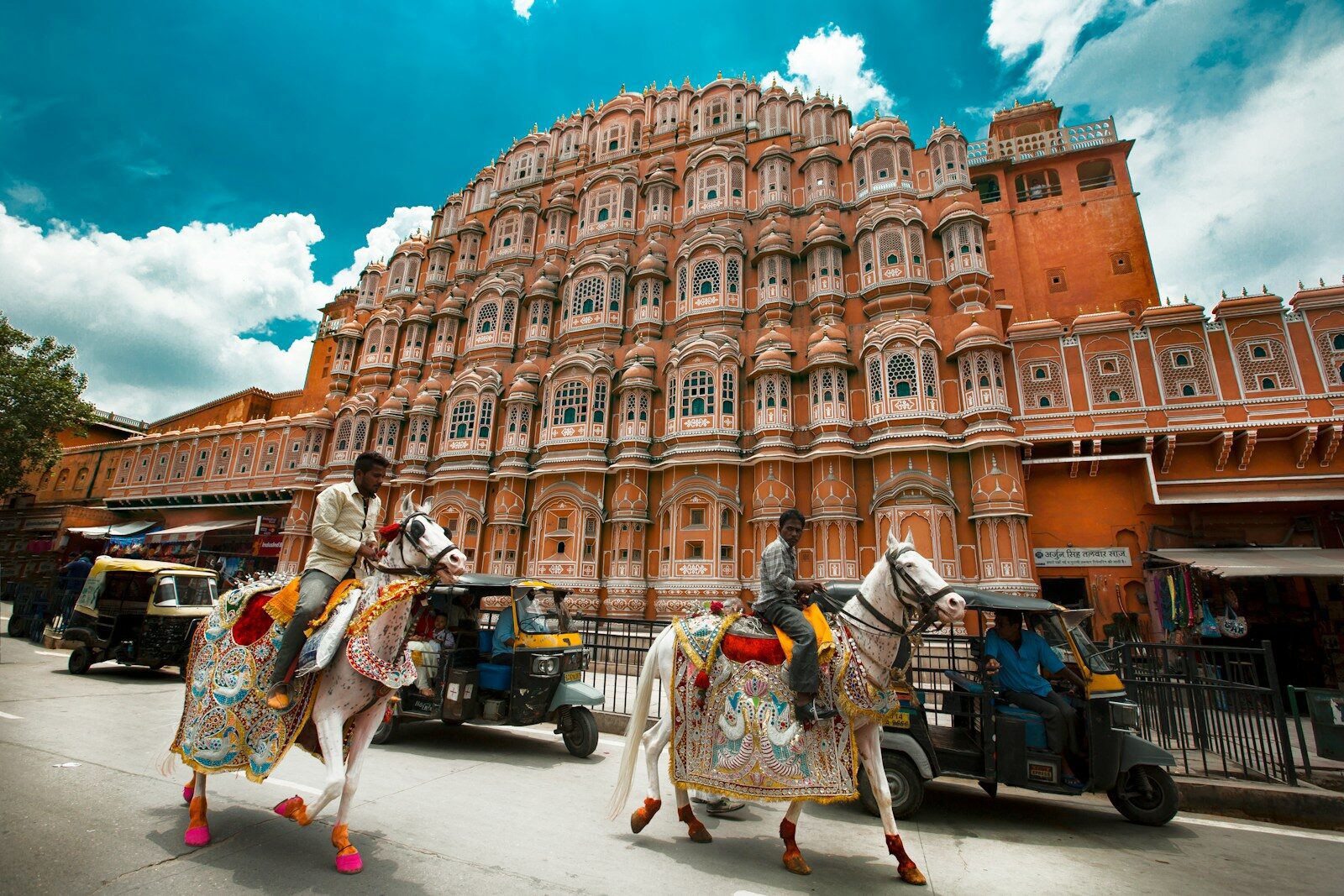 Two men riding decorated white horses past Hawa Mahal in Jaipur