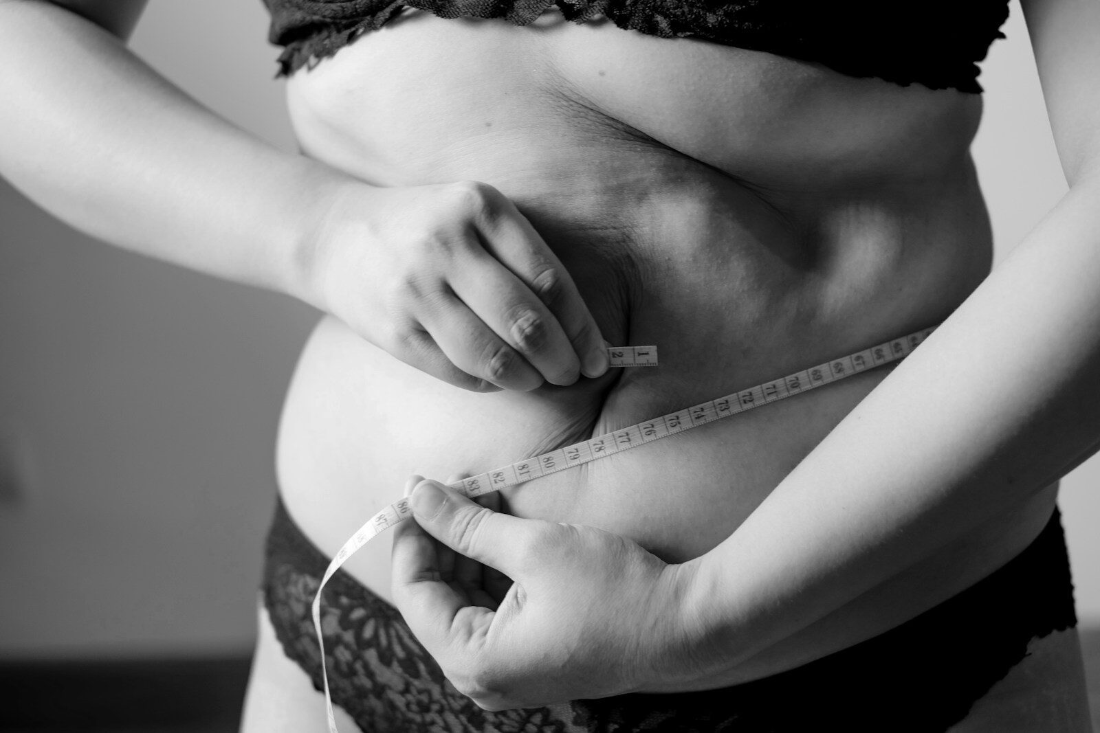 A person in black lace underwear measuring their waist with a white tape measure