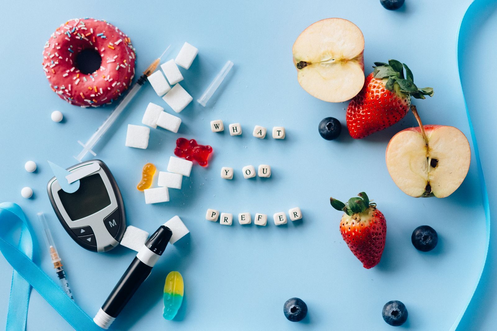 A creative diabetes awareness still life with insulin syringe, fruits, donut, and glucose meter on blue background.