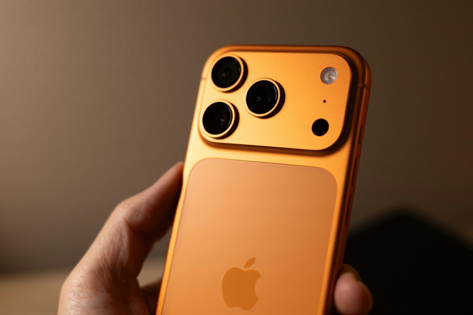 Orange smartphone with triple camera system held